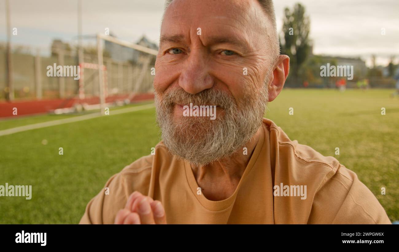 Old elderly Caucasian man stadium outside meditating on lawn sitting closed eyes smiling harmony retirement concentration wellness dreaming peaceful Stock Photo