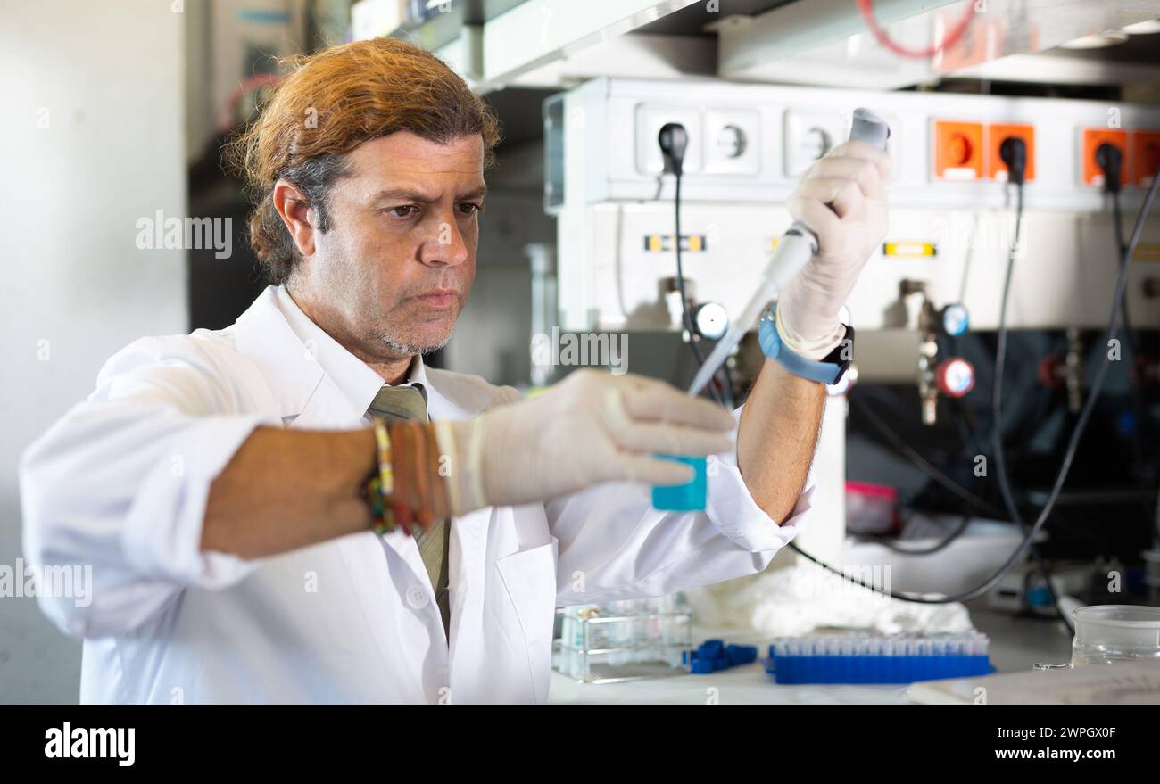 Male chemist working in laboratory, analyzing liquid samples in flasks ...