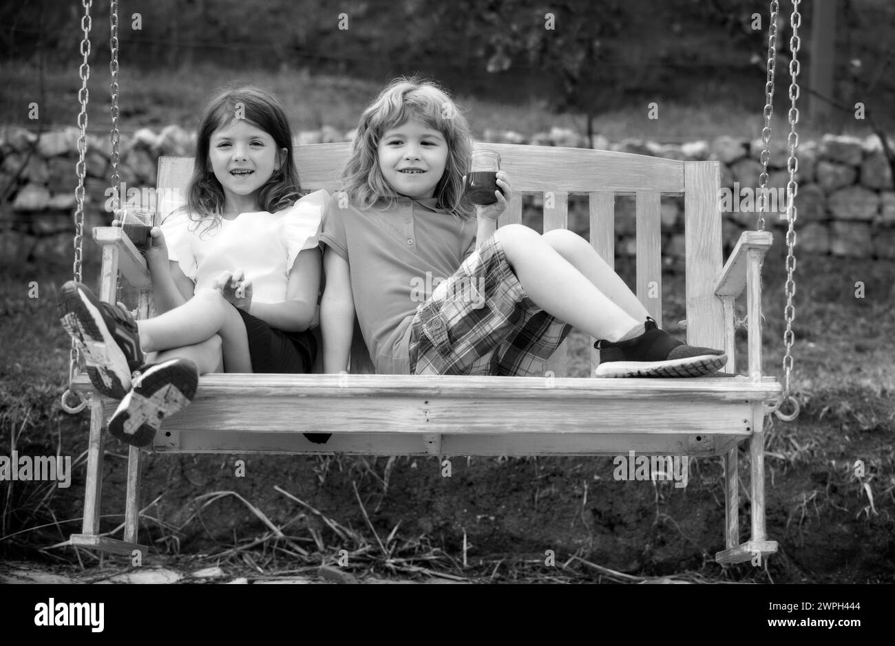 Portrait of brother and sister swinging on swing in summer park ...