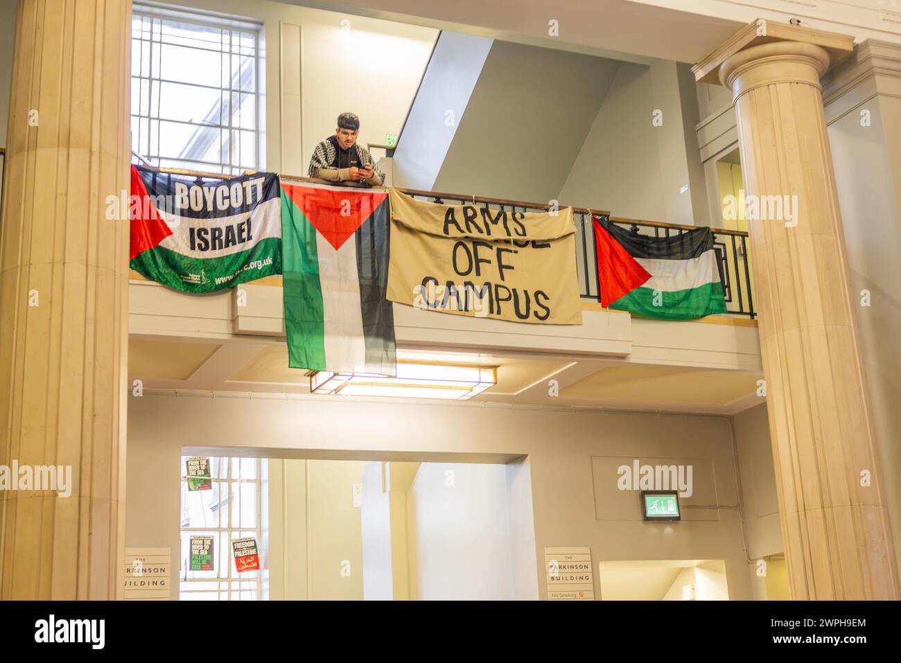 Leeds, UK. 07 MAR, 2024. Pro palestine demonstrator stands with banners on Balcony at University of Leeds. Story: Palestine protestors occupy the Parkinson building at the University of Leeds. The studends demand the suspension of Rabbi Zecharia Deutsch as a Jewish chaplain on campus, the Rabbi had temporarily left UOL to serve in the IDF and subsequently returned to campus and for the university to stop working with BAE/Israeli Universities. Protestors plan to occuply the site for the forseable future. Credit Milo Chandler/Alamy Live News Stock Photo
