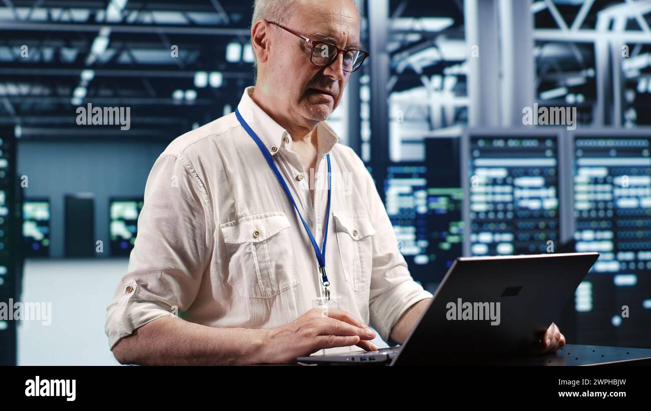 Trained engineer expertly managing data while navigating in industrial server room. Specialist ensuring errorless cybersecurity protection, optimizing systems and performing necessary updates Stock Photo