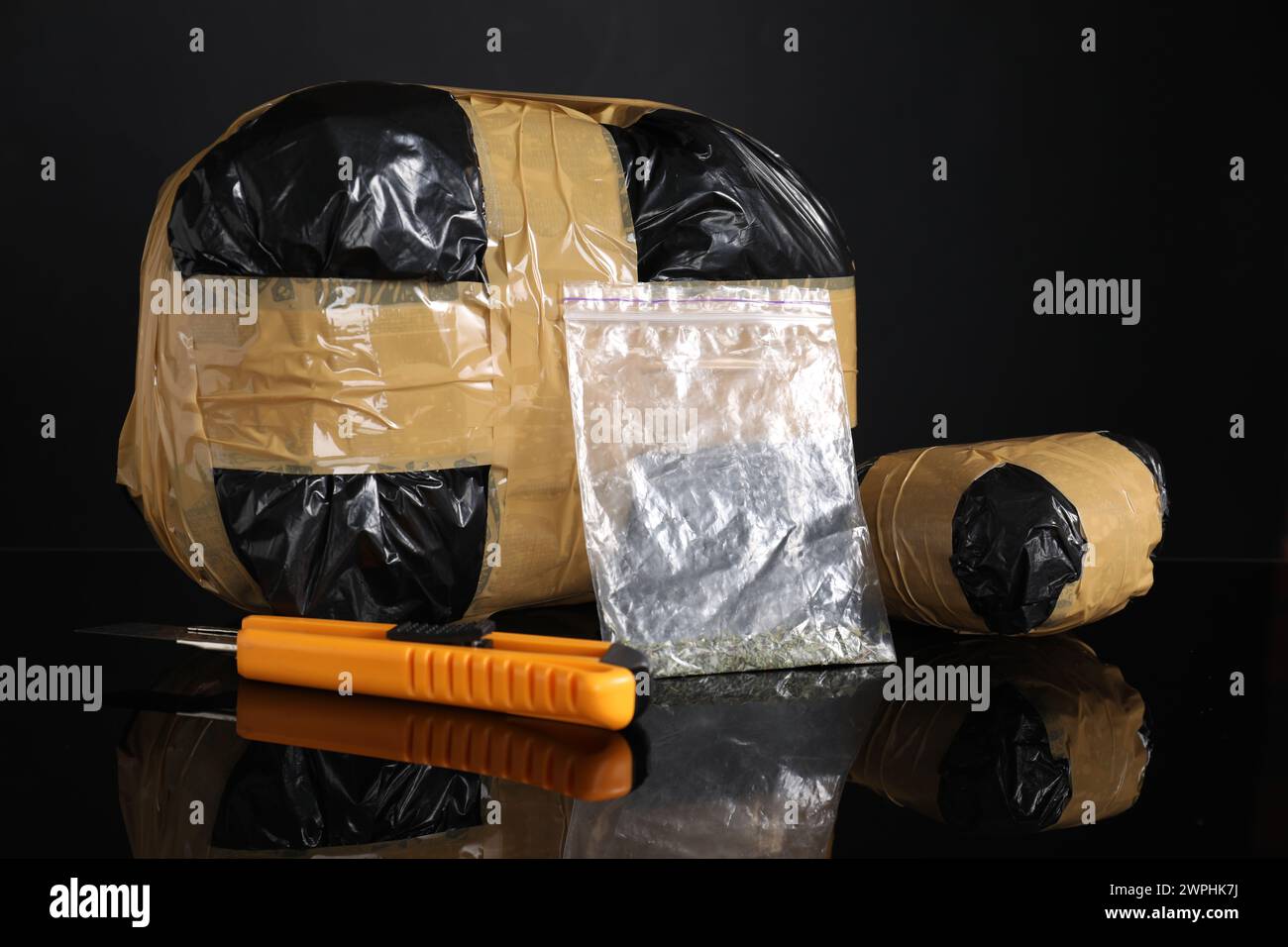 Smuggling, drug trafficking. Packages with narcotics and utility knife on black mirror surface Stock Photo