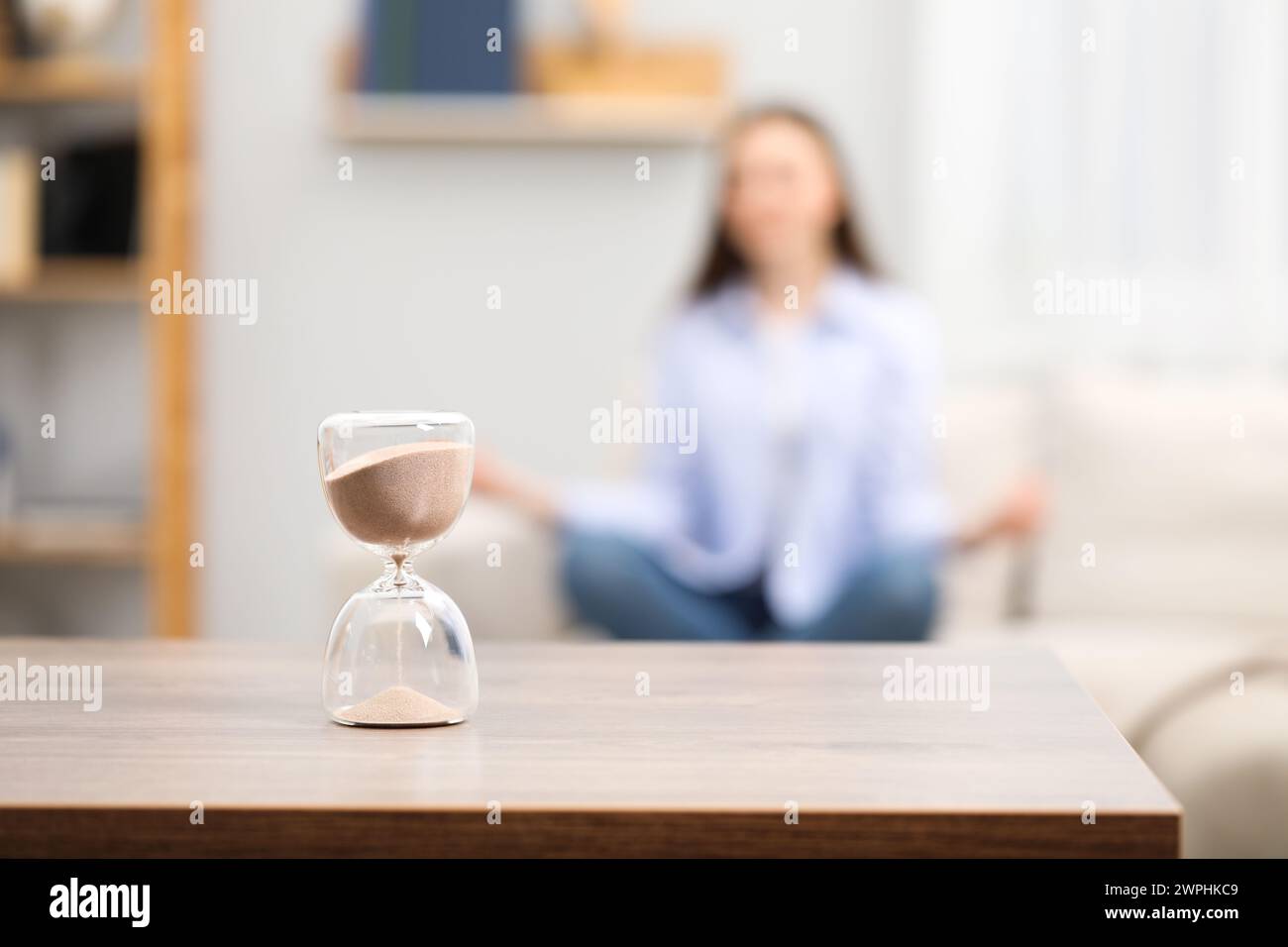 Hourglass with flowing sand on desk. Woman meditating indoors, selective focus Stock Photo