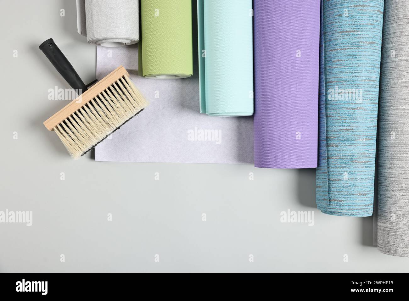 Different wallpaper rolls and brush on light background, flat lay. Space for text Stock Photo