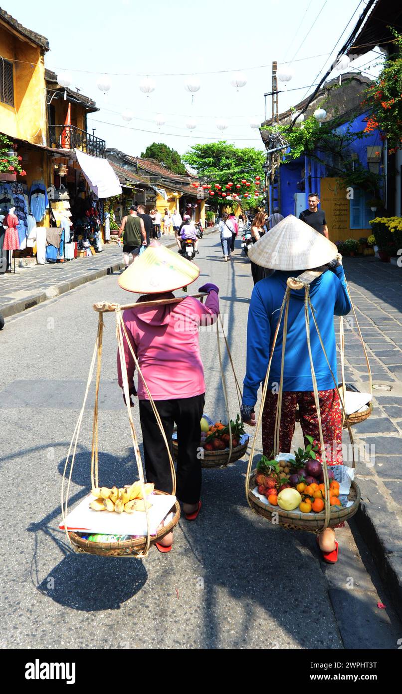 Vietnamese women walking with carrying pole with baskets with fruits, also called a shoulder pole, in Hoi An, Vietnam. Stock Photo