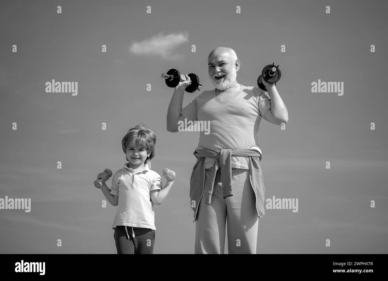 Funny old senior man and kid boy with dumbbells. Healthcare cheerful lifestyle. Active family enjoy sport and fitness. Stock Photo