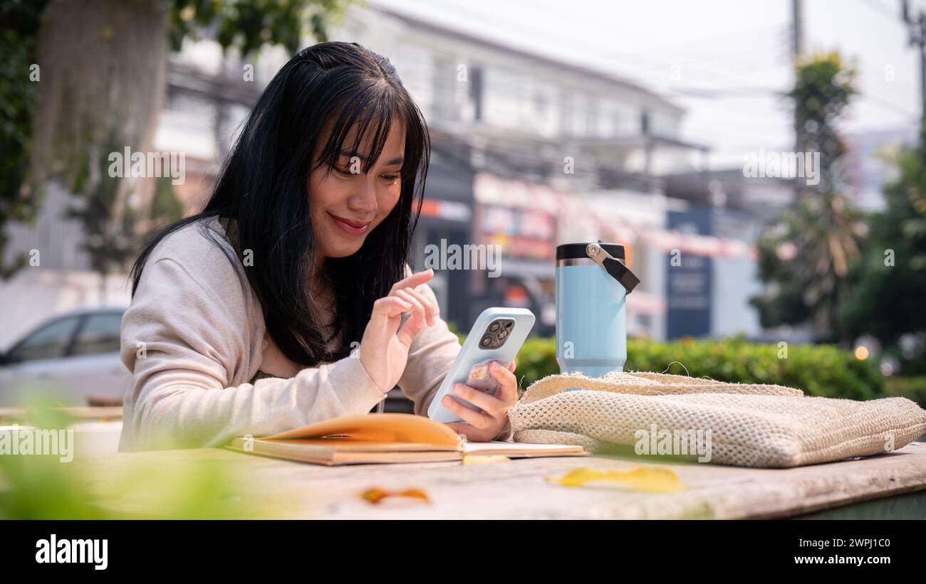 An attractive, happy Asian woman sitting at a table outdoors in the ...