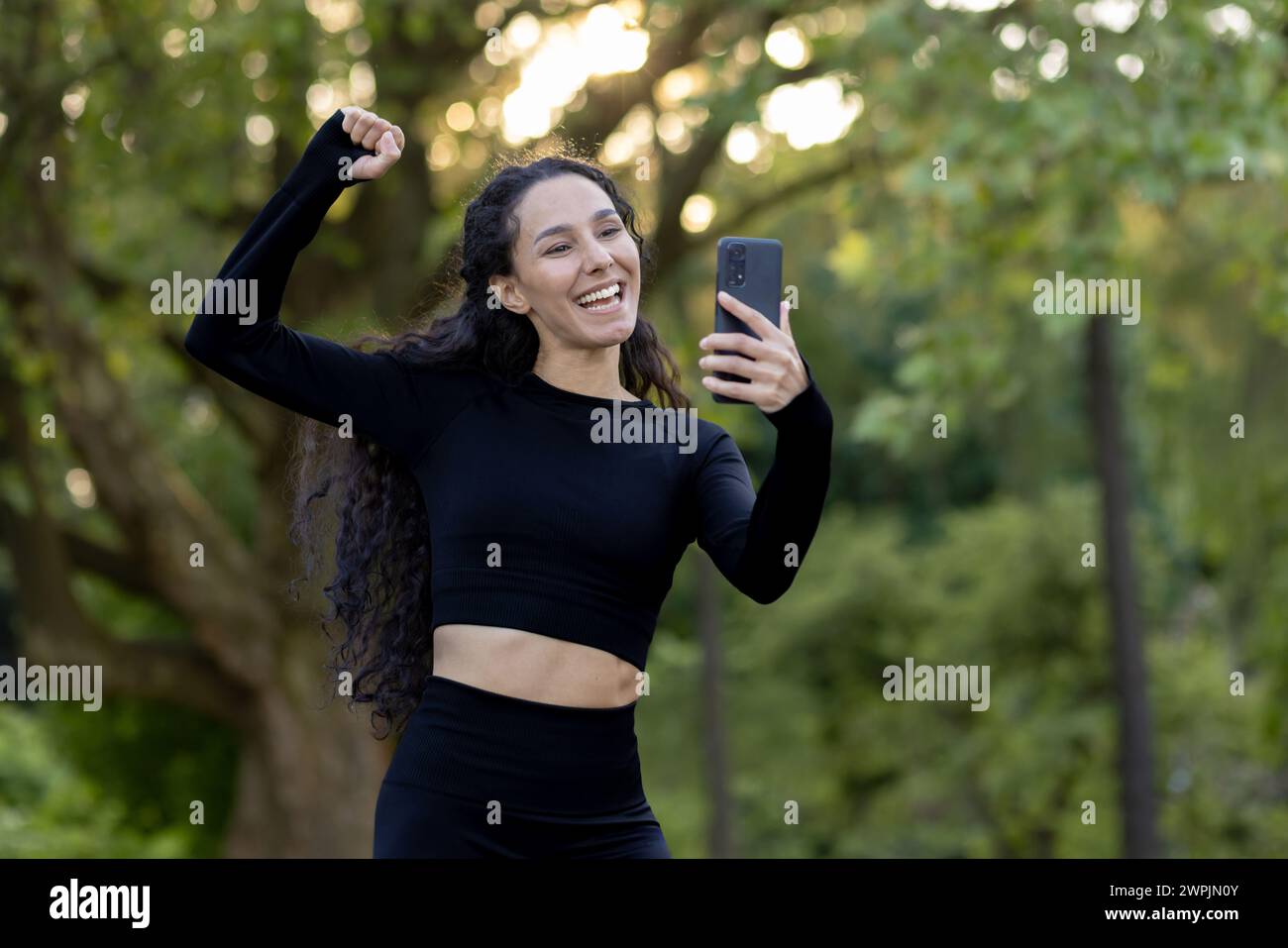 Smiling, active female in athletic attire captures a cheerful moment on her phone, embodying health and happiness. Stock Photo