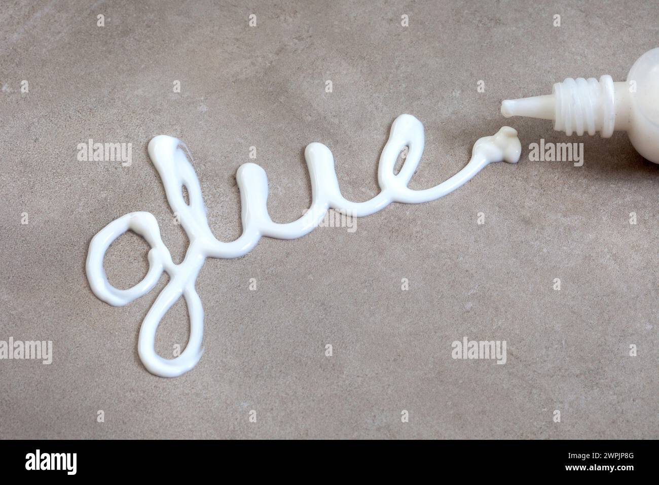 The word glue written with white wood glue on a mottled grey surface with copy space Stock Photo