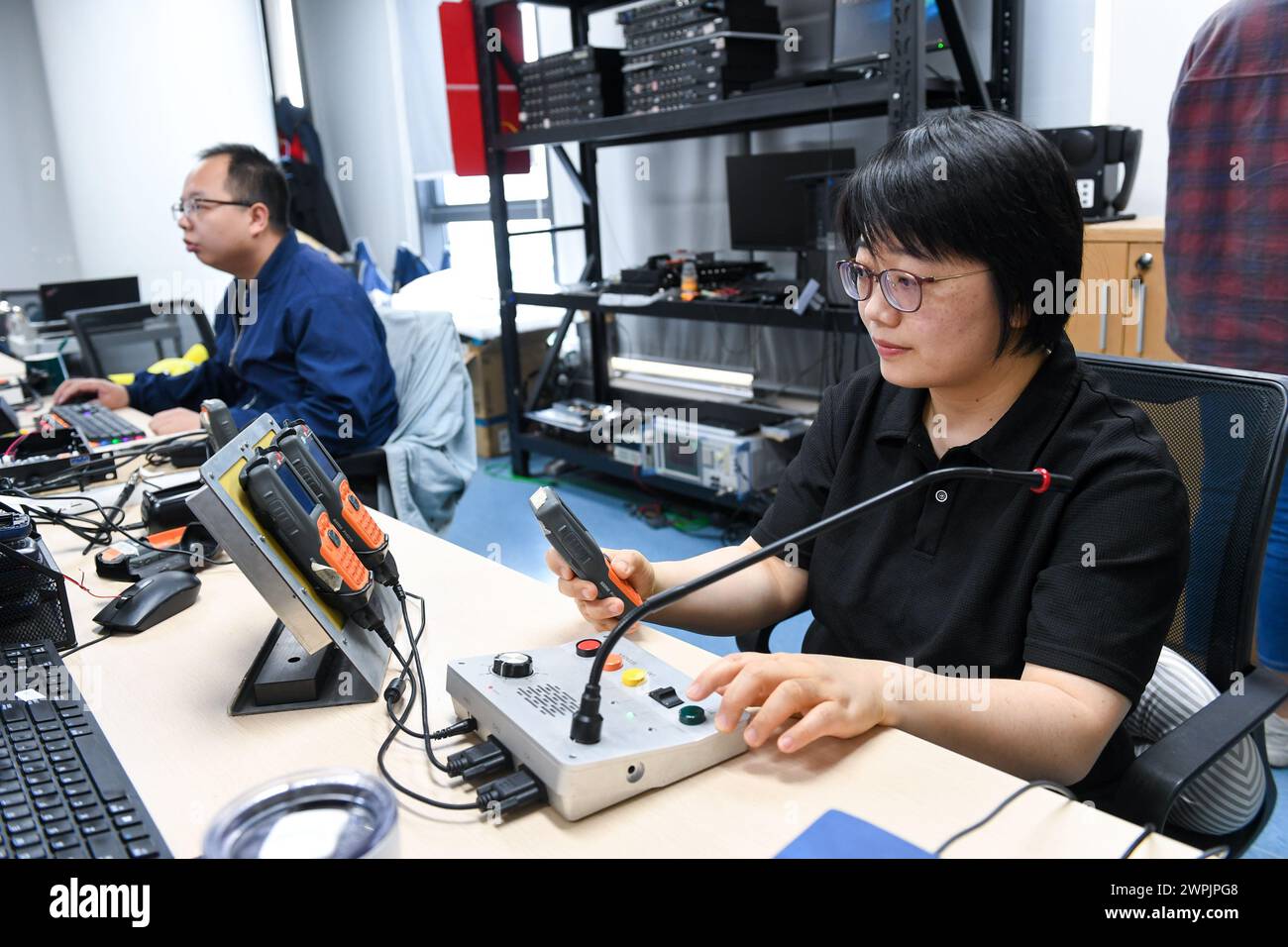(240308) -- SHENZHEN, March 8, 2024 (Xinhua) -- Chen Shuxian (R) tests equipment at an office in Shenzhen, south China's Guangdong Province, Feb. 20, 2024. Chen Shuxian is a technical director of the wireless software test group of Shenzhen SED Wireless Communication Technology Co., Ltd. Her office is filled with small brick-like handhelds, which are mainly used for wireless communication in rail traffic. 'I feel a sense of fulfillment every time I see the conductors of high-speed trains using the handhelds,' Chen said. After joining the company in 2008, Chen participated in the research a Stock Photo