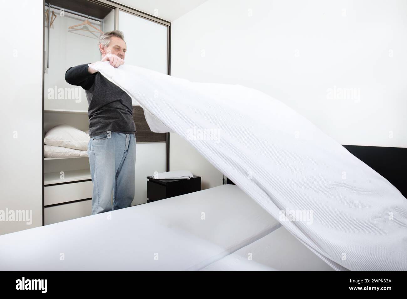 Older man working in bedroom on making bed Stock Photo