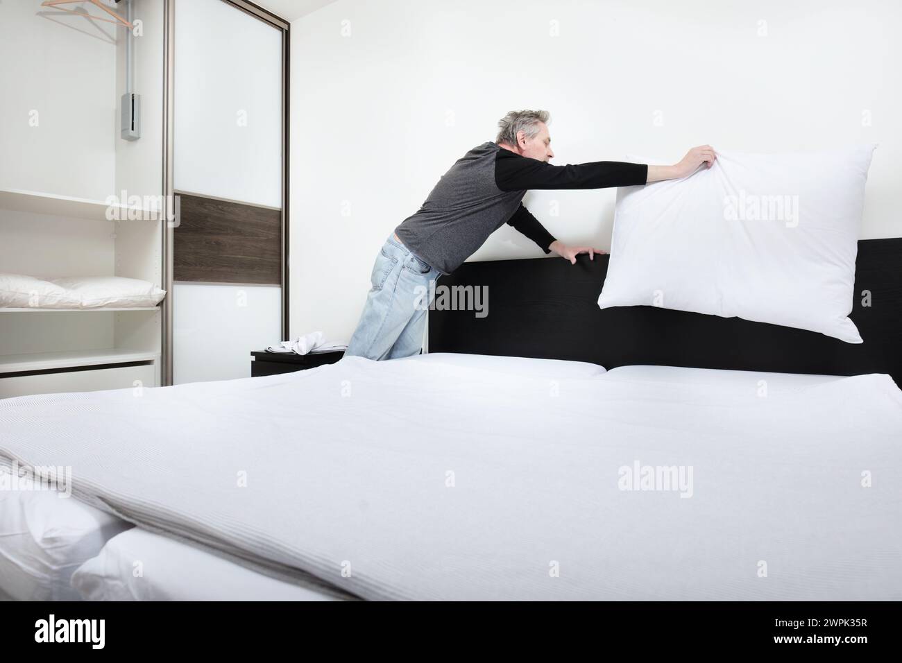 Older man working in bedroom on making bed Stock Photo