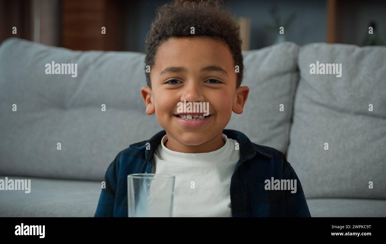 Head shot close up portrait little funny cute 10s kid boy ethnic child drink milk at home smiling to camera with crooked teeth. African American son Stock Photo