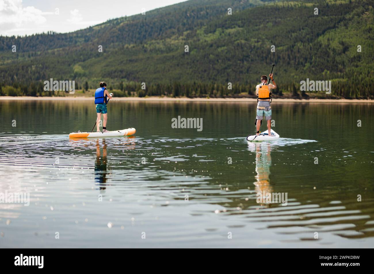 Two paddleboarders enjoy a serene paddle on a calm mountain lake Stock Photo
