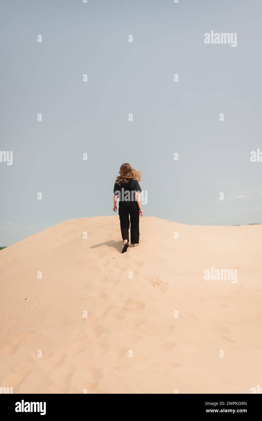 Back view of woman hiking up sand dunes with hair flowing in the wind Stock Photo
