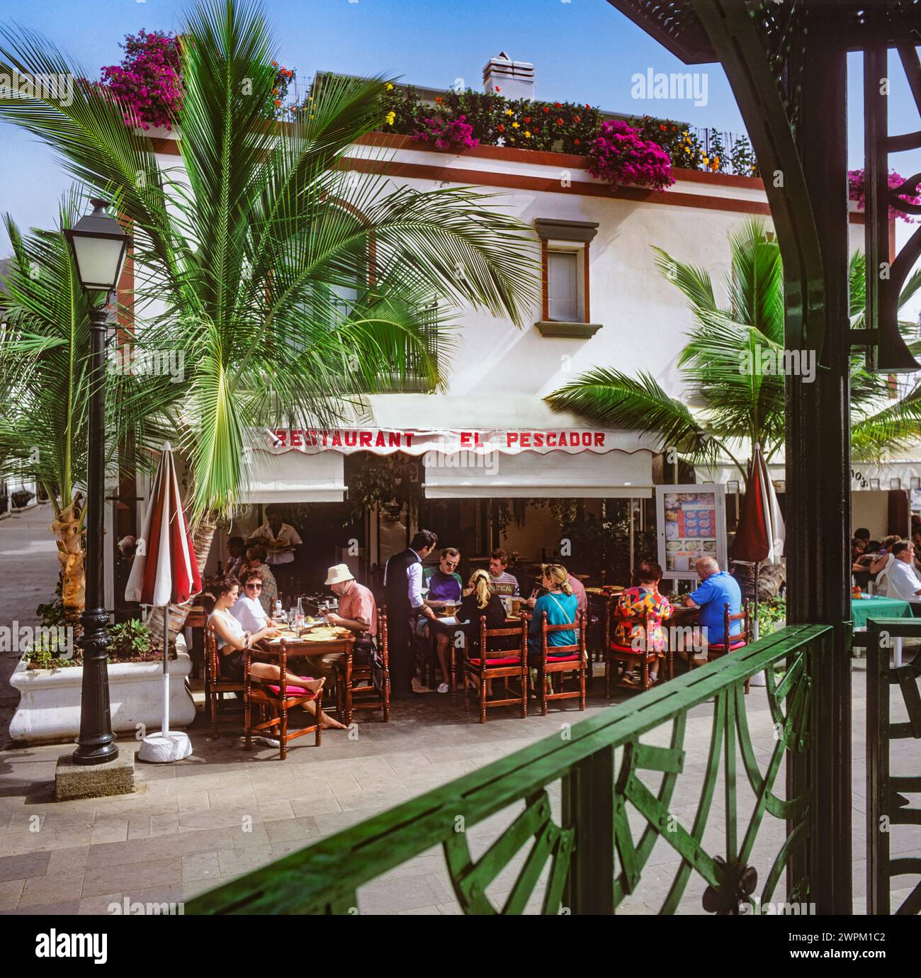 1980s Spain Retro Travel with alfresco Spanish restaurant exterior, waiter serving Spanish tapas to tourists on terrace of typical Puerto de Mogan restaurant viewed from bandstand Gran Canaria Canary Islands Spain Stock Photo