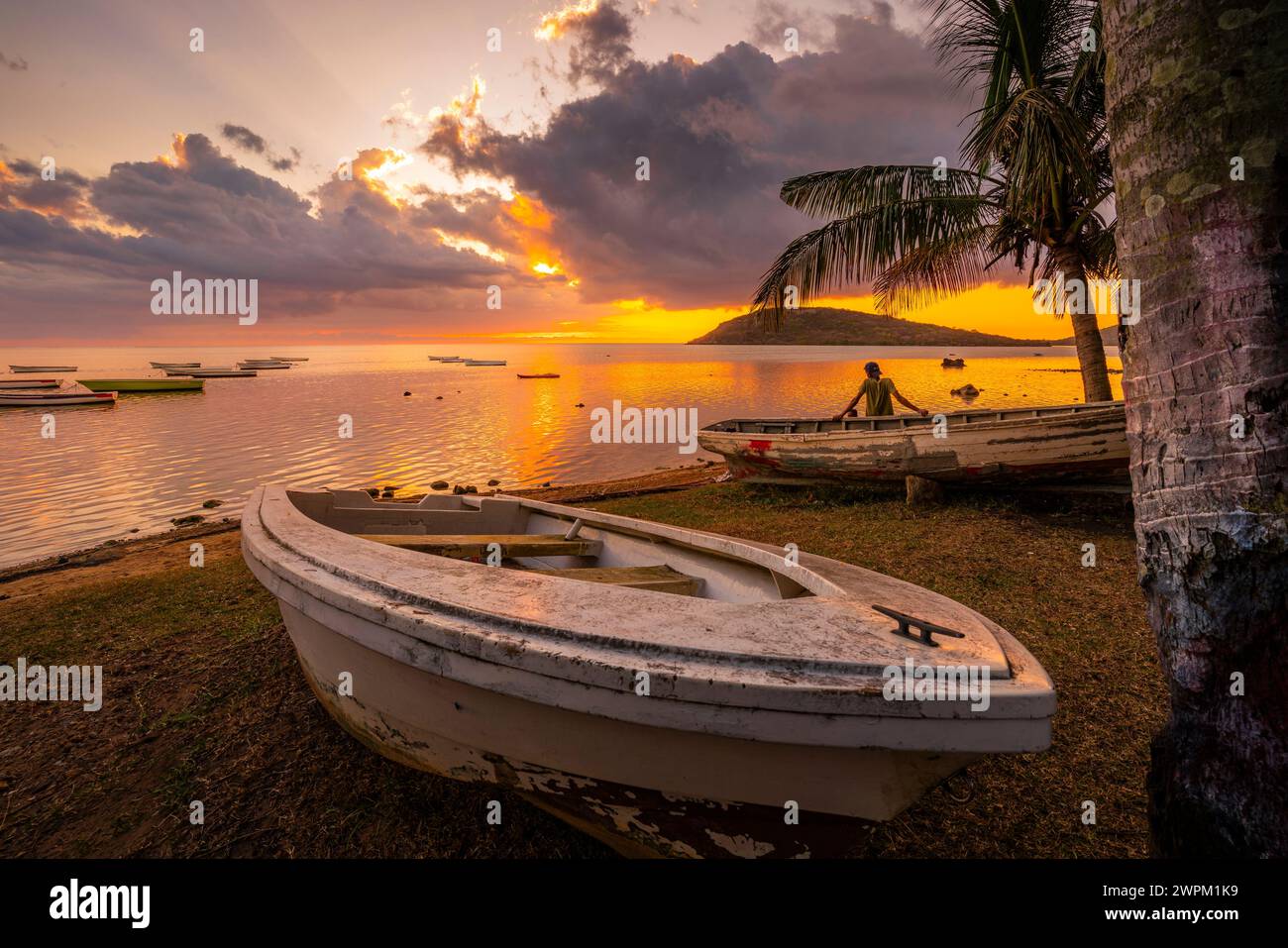 View of local man sat on boat viewing Le Morne from Le Morne Brabant at sunset, Savanne District, Mauritius, Indian Ocean, Africa Stock Photo