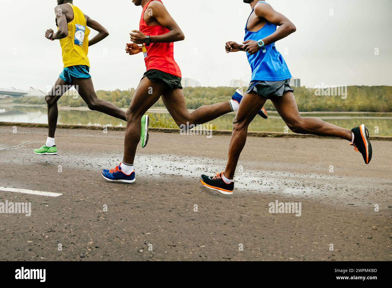 leading group african runners dressed in bright sports clothes race along calm river, summer marathon Stock Photo