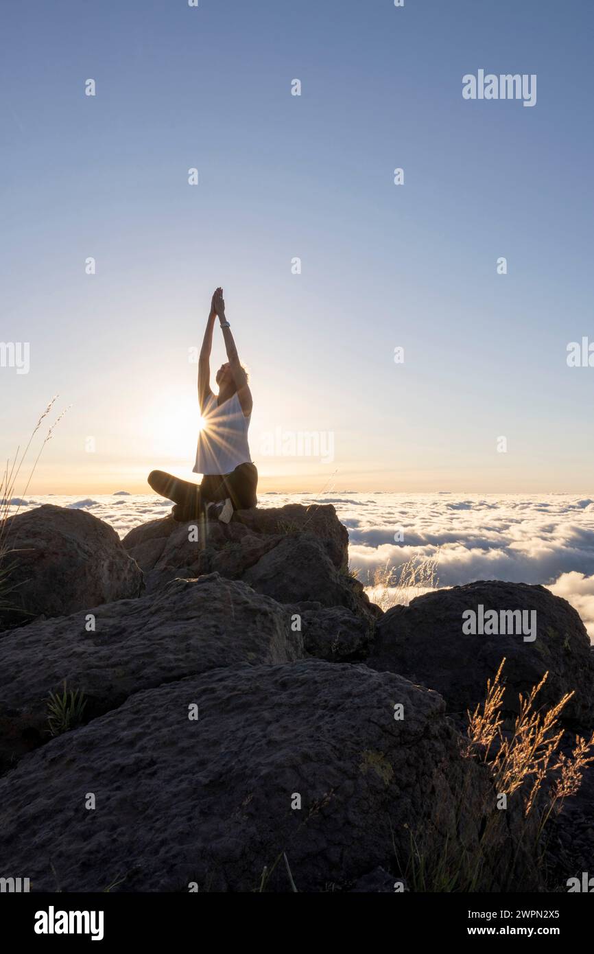 Woman doing yoga and relaxation exercises at sunrise above the clouds, Miradouro do Pico do Areeiro, Madeira, Portugal, Europe Stock Photo