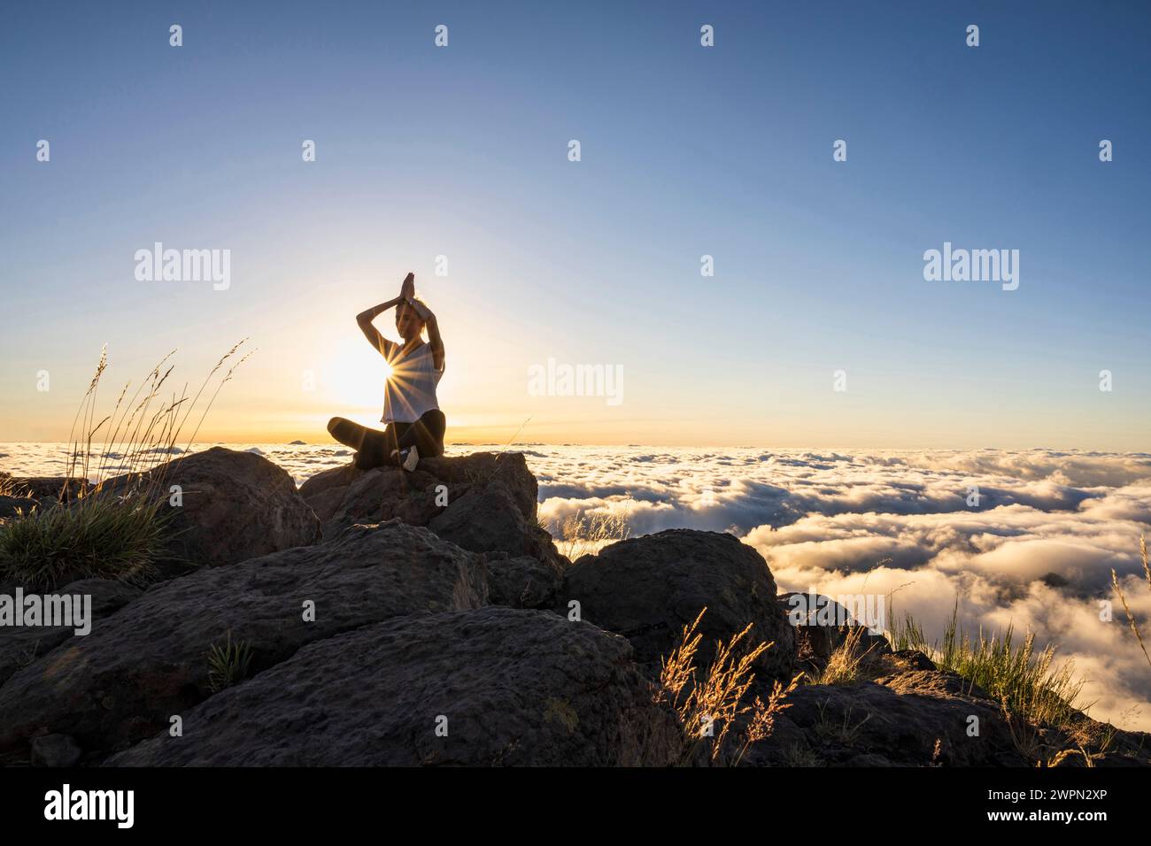 Woman doing yoga and relaxation exercises at sunrise above the clouds, Miradouro do Pico do Areeiro, Madeira, Portugal, Europe Stock Photo