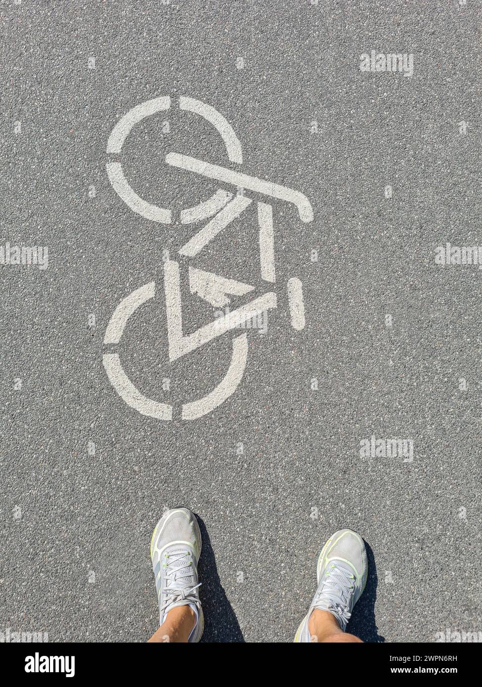 Women's legs with white sports shoes in front of bicycle pictogram on a cycle path in Germany Stock Photo