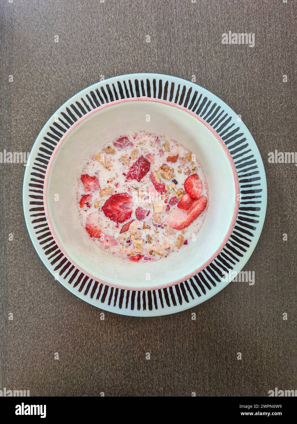 Dried small red slices of strawberries in muesli with milk in a bowl Stock Photo