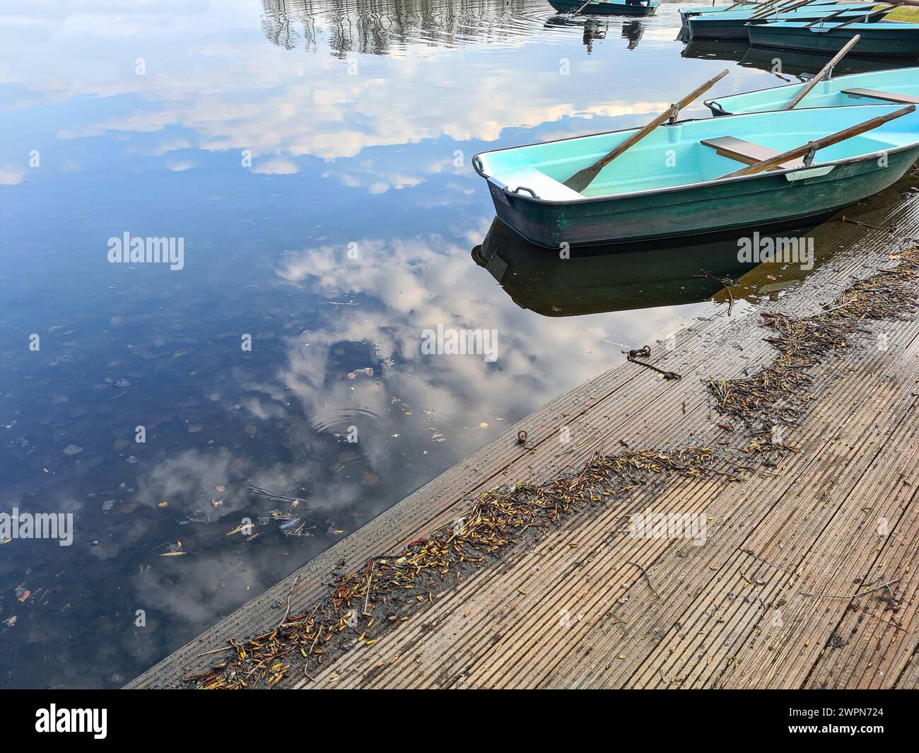 View of a rowing boat on a wooden jetty on a lake with fair weather clouds reflecting in the water, atmospheric ambience Stock Photo