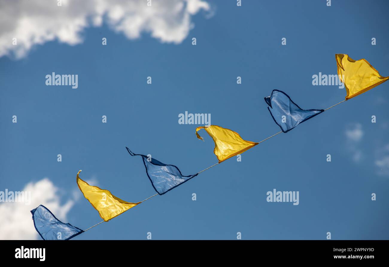 Yellow and blue triangular festival flags on sky background with white clouds. Outdoor Celebration Party. Festive mood Stock Photo