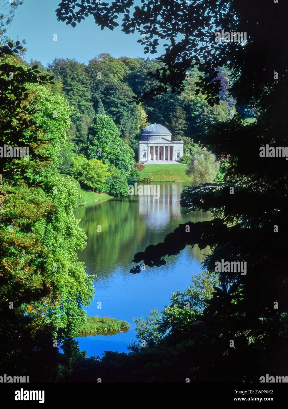 Glimpse view between trees of the lake and Pantheon in landscaped gardens at Stourhead, Wiltshire, England, UK Stock Photo