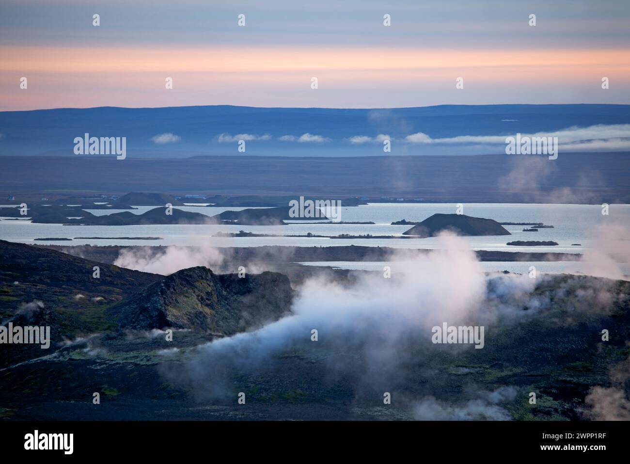 Steam clouds glowing in the evening sun from the Jardbadsholar crater in the geothermal area at Namafjall. View over Lake Myvatn. Stock Photo