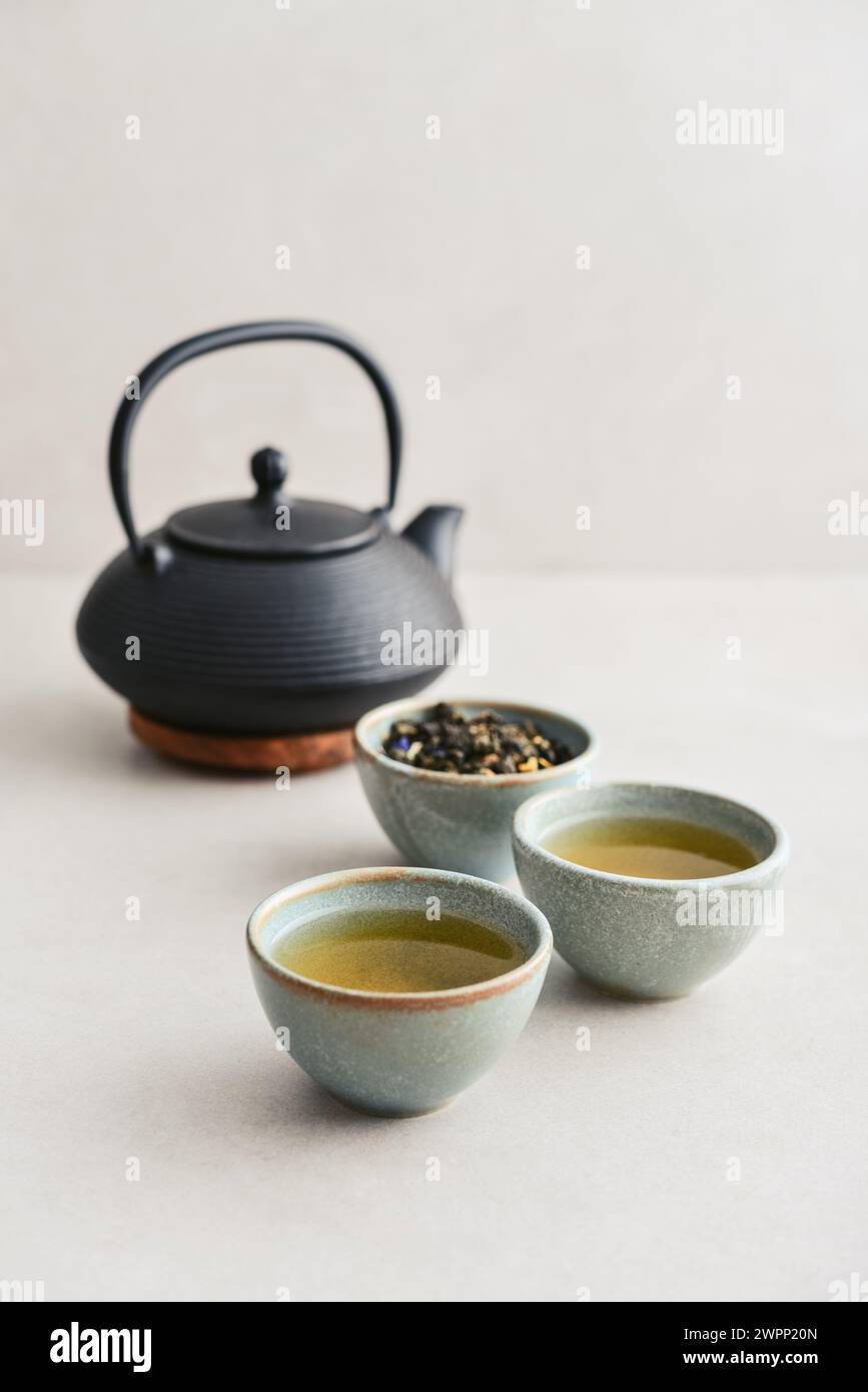 Black cast iron teapot and two ceramic cups of green tea on a light background Stock Photo