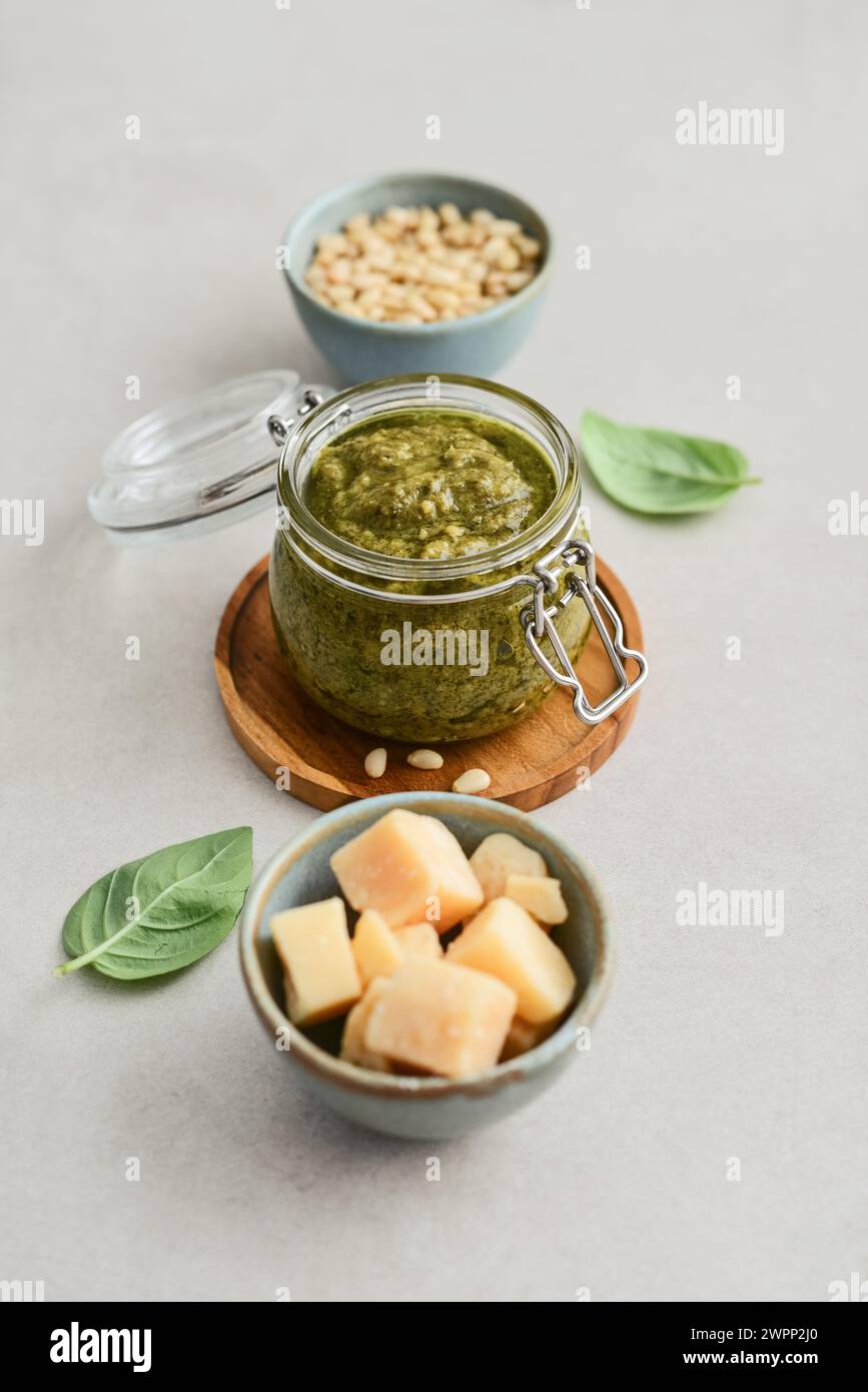 Sauce pesto in glass jar with fresh basil, hard cheese and pine nuts on light background Stock Photo