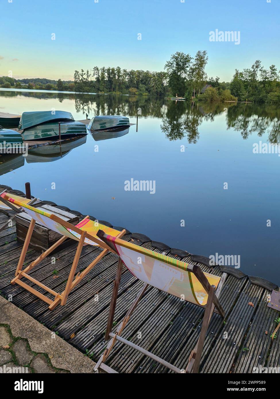 Two deckchairs on a wooden jetty on the shore with a view of boats ...