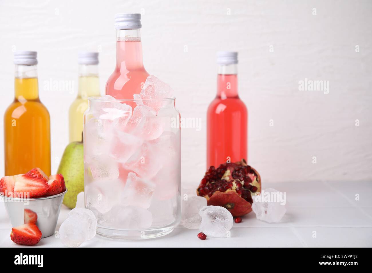 Tasty kombucha in bottles, glass with ice and fresh fruits on white table, space for text Stock Photo