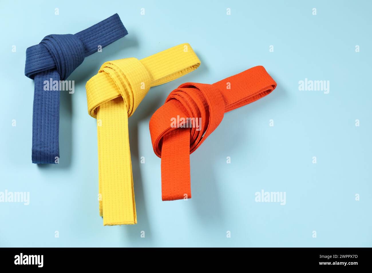 Colorful karate belts on light blue background, flat lay. Space for ...