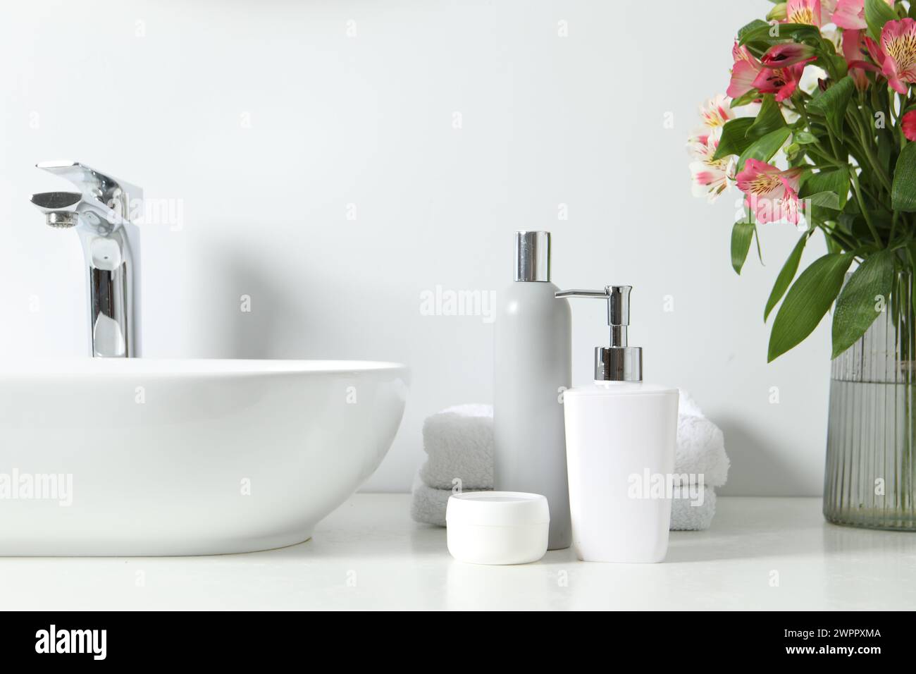 Vase with beautiful Alstroemeria flowers and toiletries near sink in bathroom Stock Photo