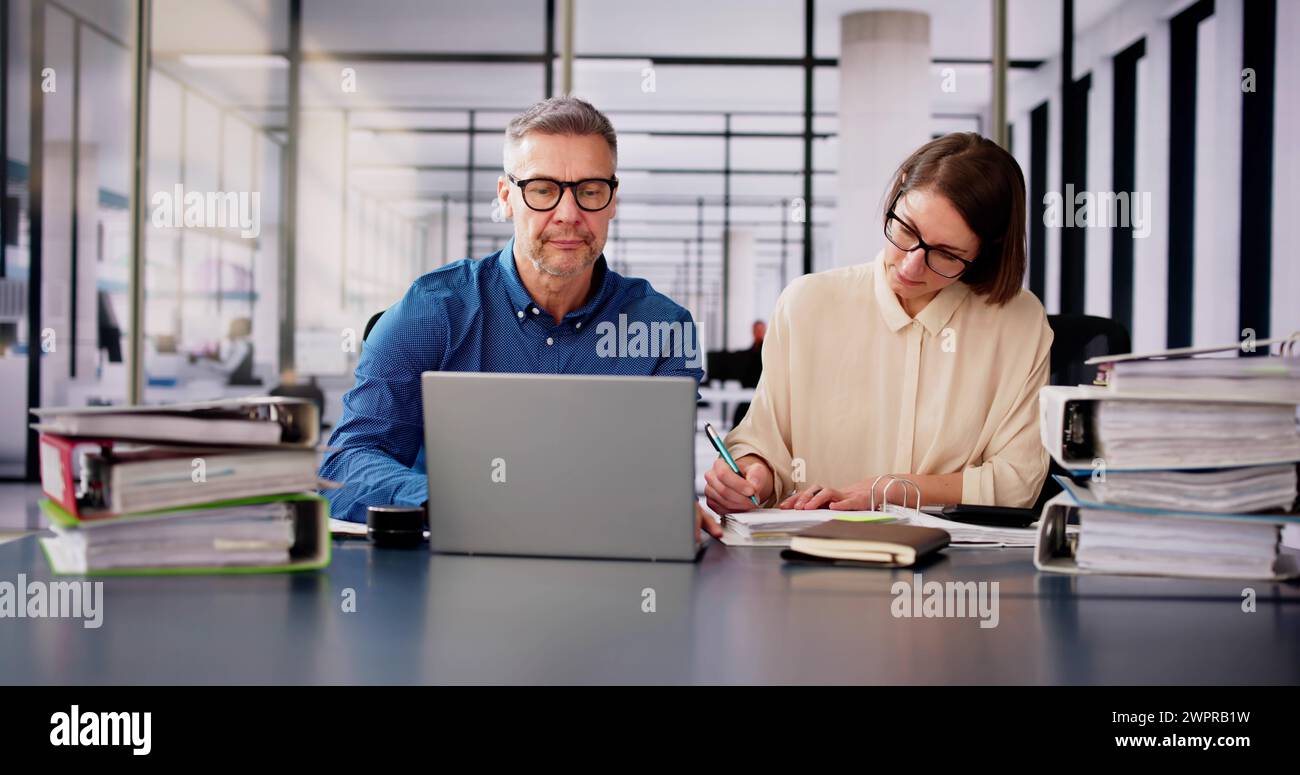 Two Businesspeople Calculating Invoice In Office While Using Laptop Stock Photo