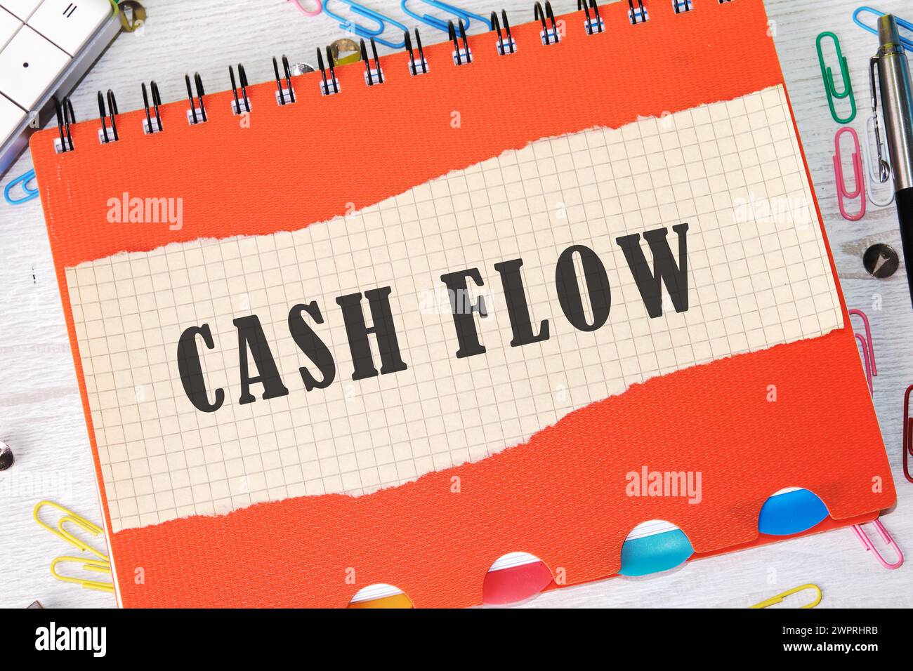 Cash flow text written on a piece of paper in a cage on the background of an orange notebook cover Stock Photo