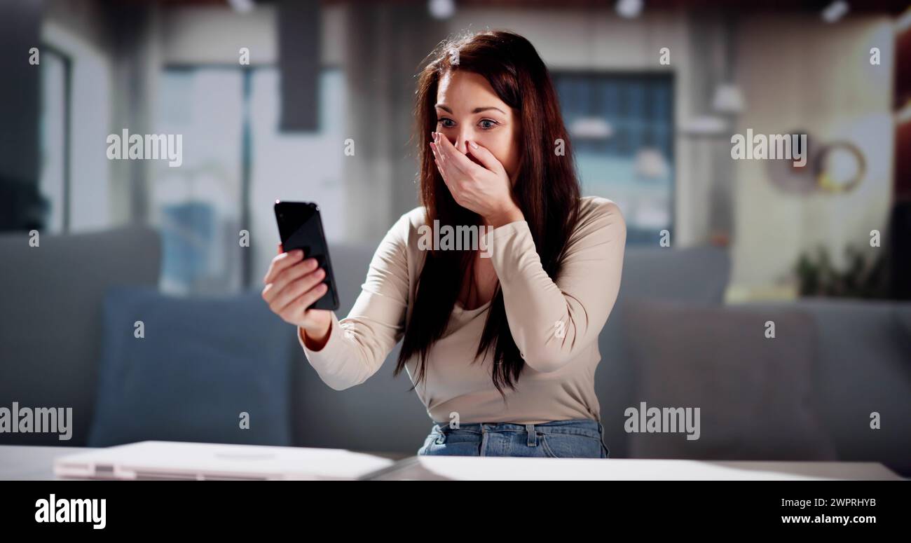Worried Young Woman Looking At Smartphone And Sitting In Front Of Sofa At Home Stock Photo