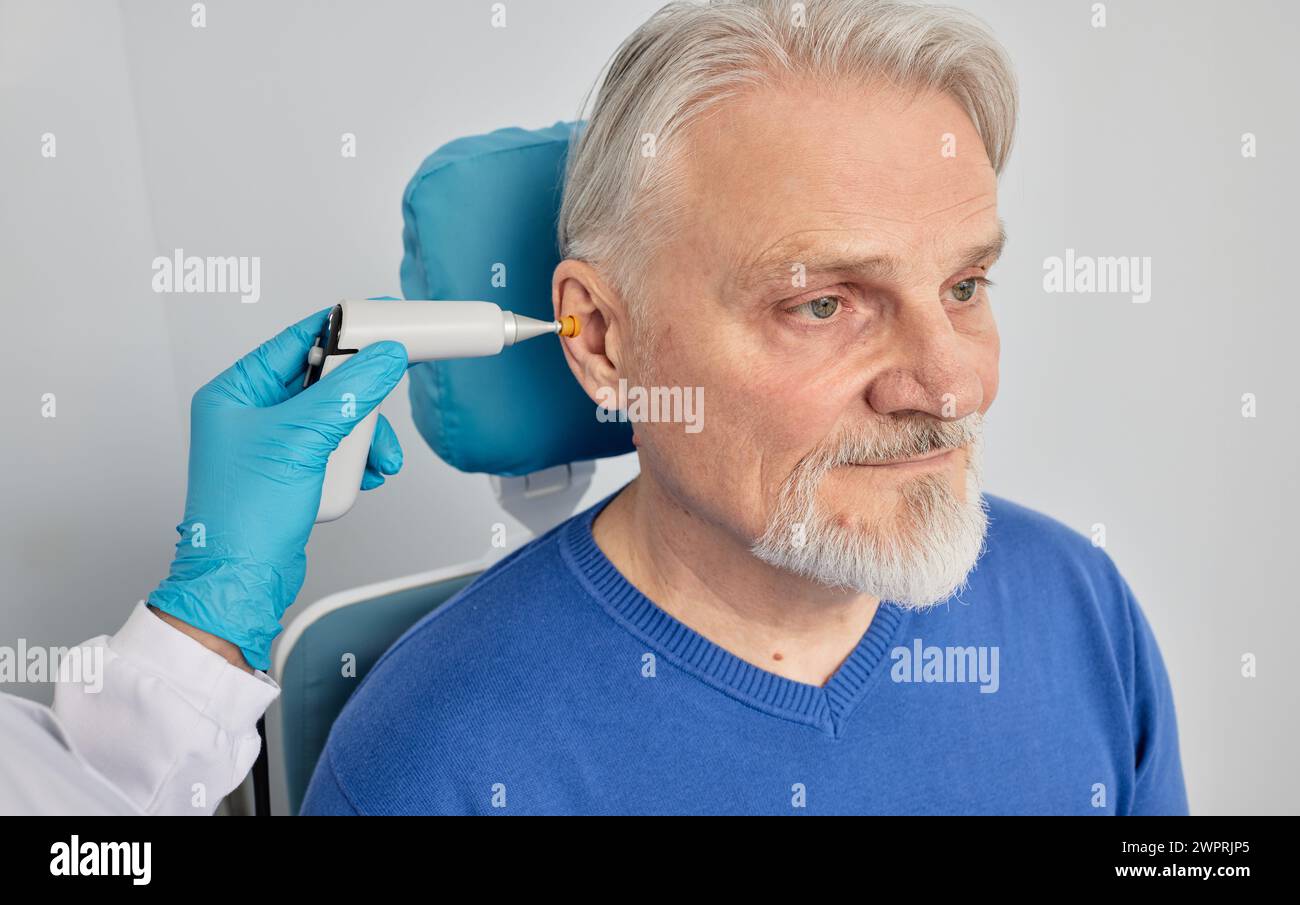 Elderly man receives tympanometry with tympanometer probe at hearing