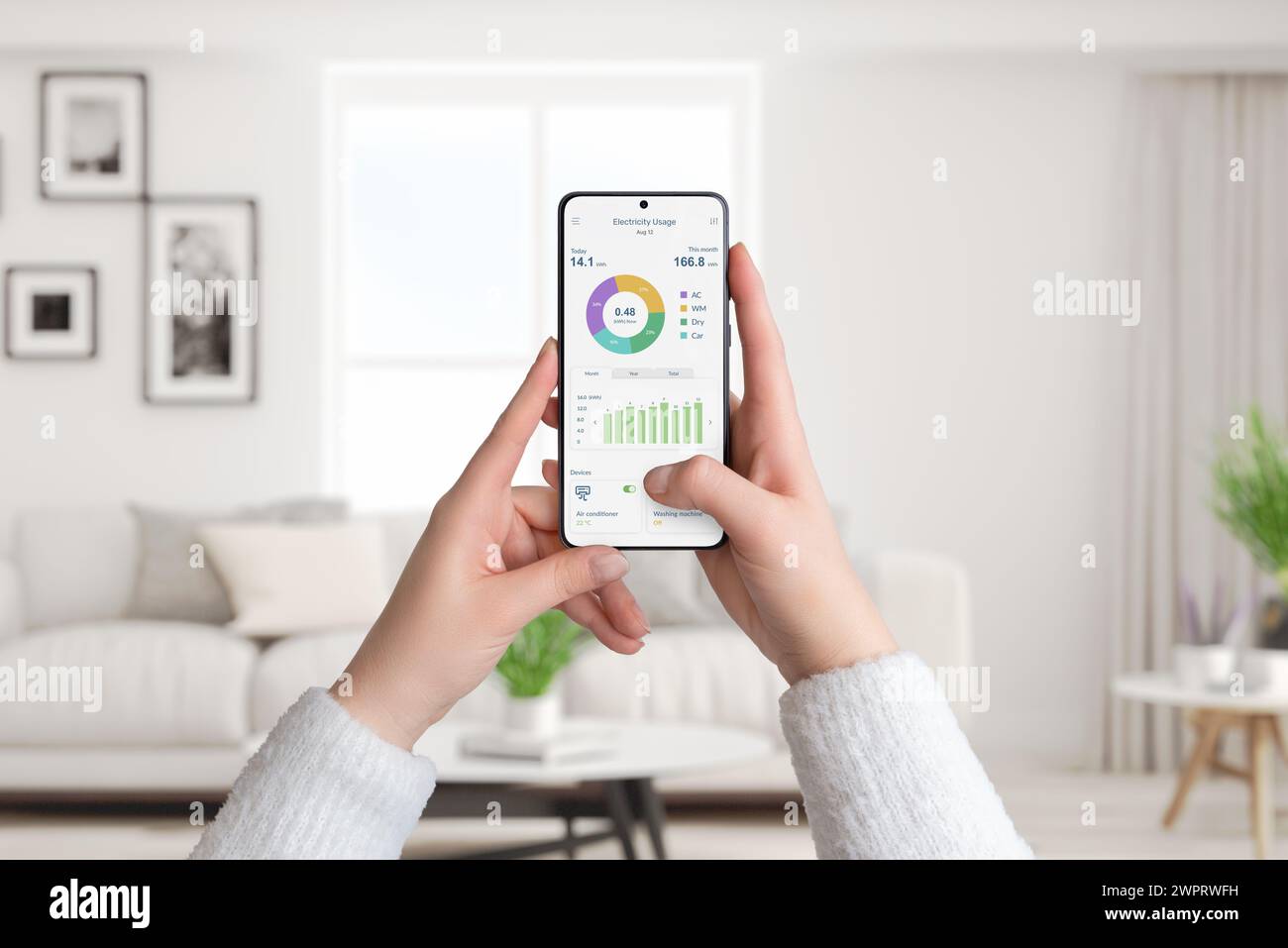 Woman holds smartphone with electricity usage app, monitoring and analyzing consumption for smart home. Living room background. Concept of energy effi Stock Photo