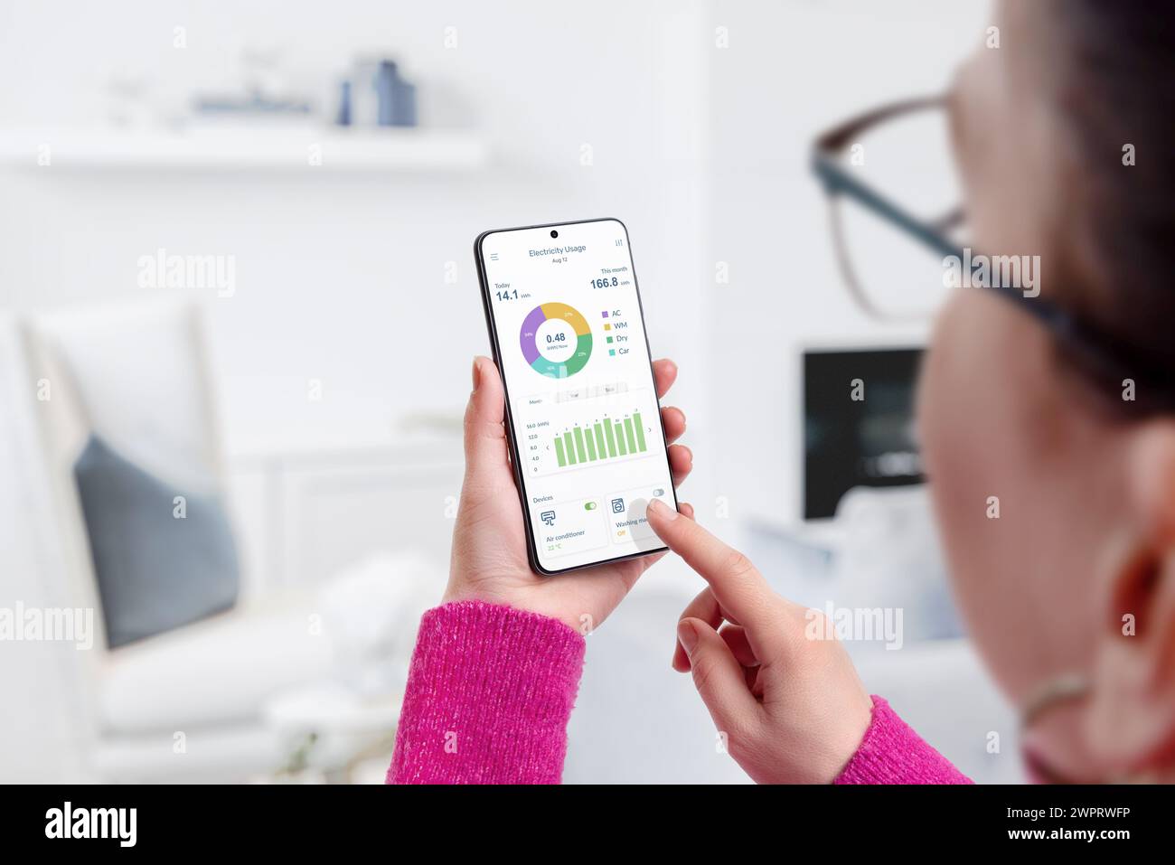 Woman uses electricity usage app for consumption monitoring and analysis in living room. Concept of energy management and smart living Stock Photo