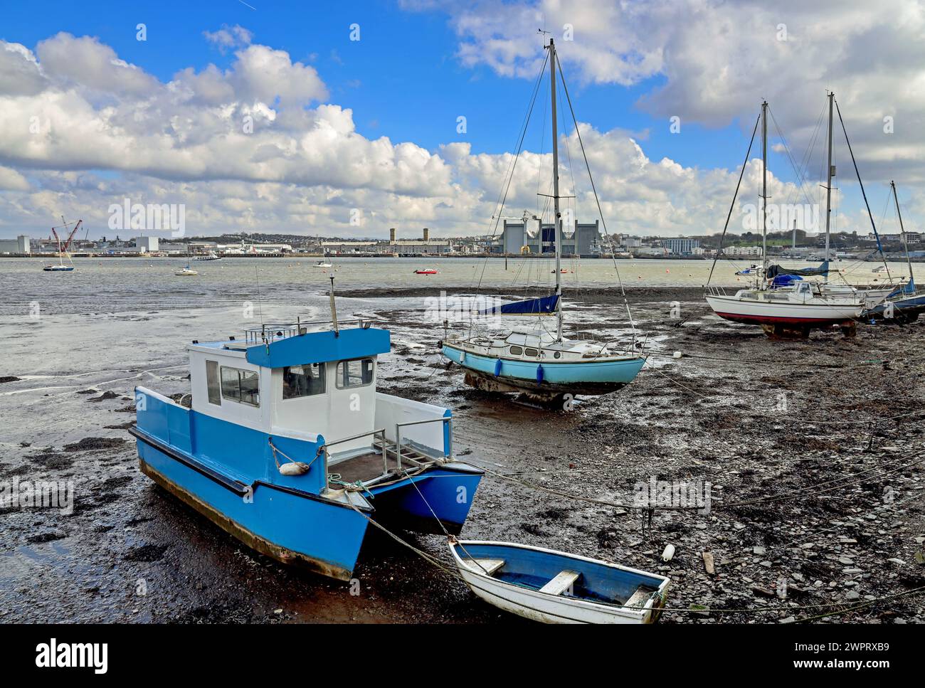 The riverside at Torpoint in south east Cornwall, with boats berthed on banks of the River Tamar. Devonport Dockyard seen acroos the water. Stock Photo