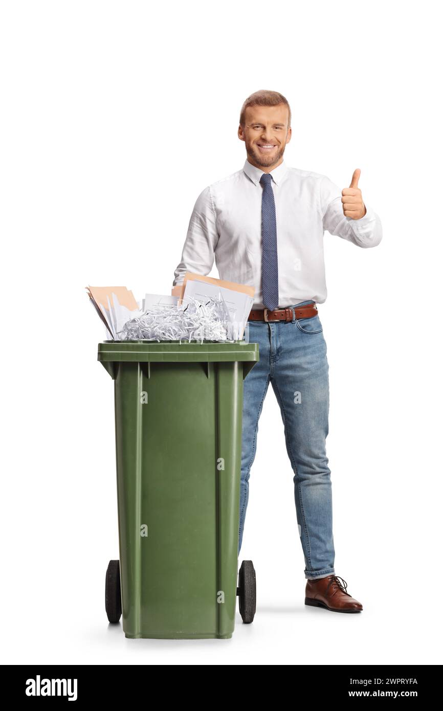 Businessman standing behind a bin with paper waste and gesturing thumbs up isolated on white background Stock Photo