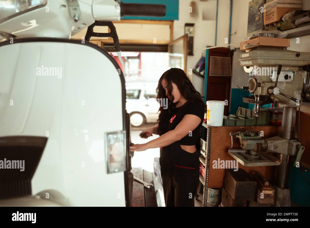 Mechanic standing by a classic scooter in a sunlit workshop full of tools, latino female in traditional masculine jobs concept, feminine power in Stock Photo