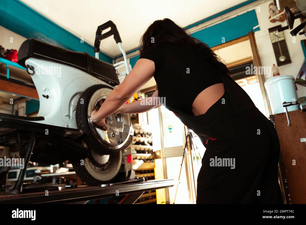 Concentrated woman mechanic working on installing a tire onto a classic italian scooter, latino female in traditional masculine jobs concept Stock Photo