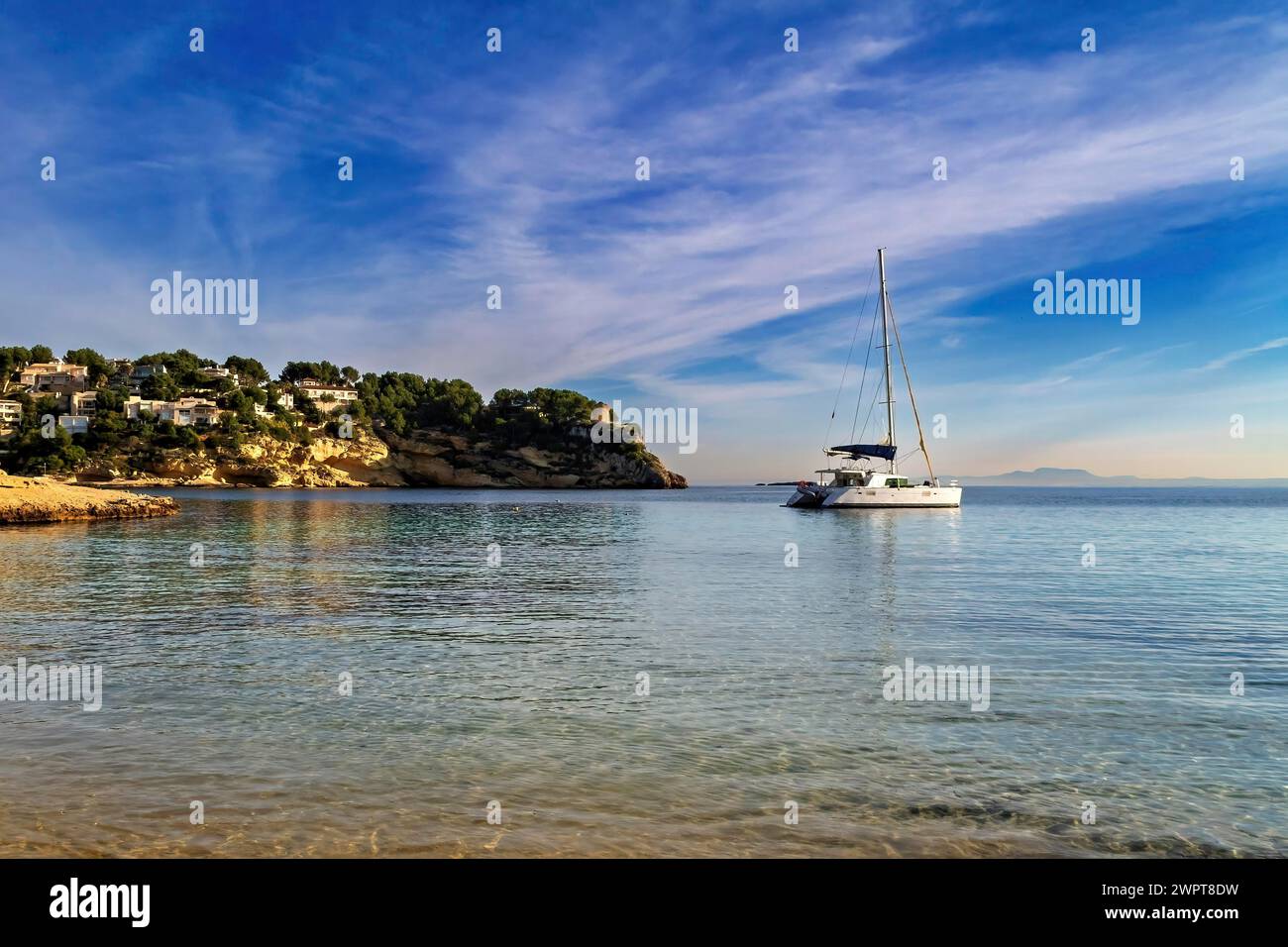 Yacht anchored near the beach with coastal homes under a sunset sky, Coastal Hiking tour in the south of Mallorca Stock Photo