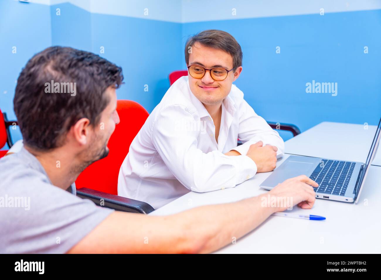 Happy and relaxed man with down syndrome and teacher talking during IT computing class Stock Photo