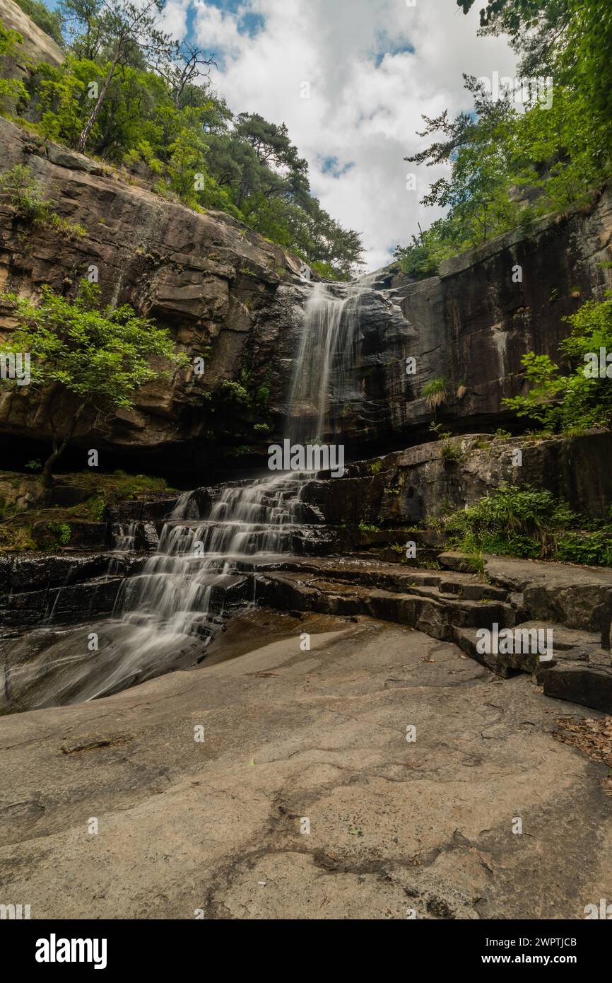 A serene waterfall cascades over rocky ledges surrounded by lush ...