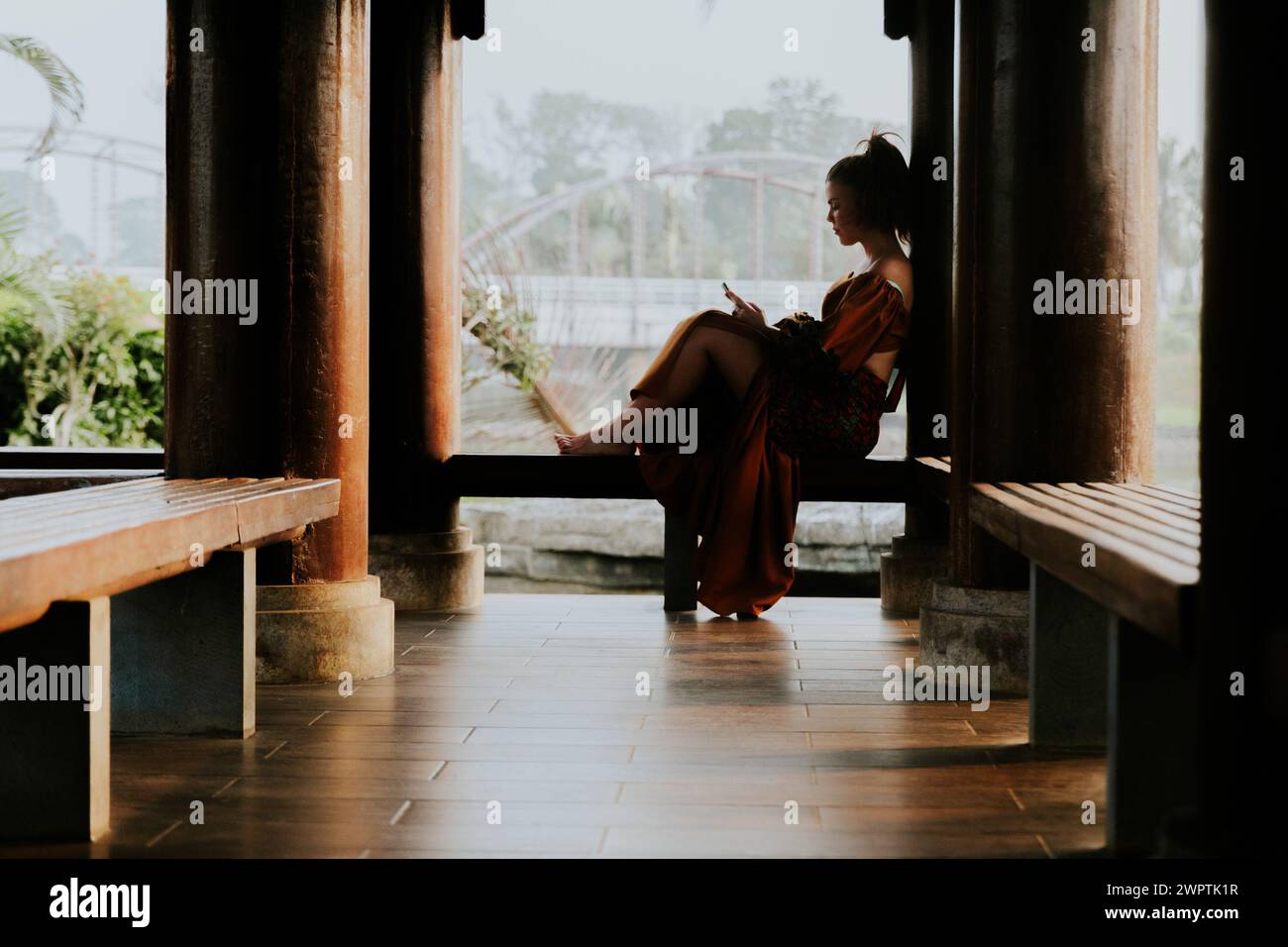 Silhouette of a girl using her smartphone sitting on a bench. Stock Photo